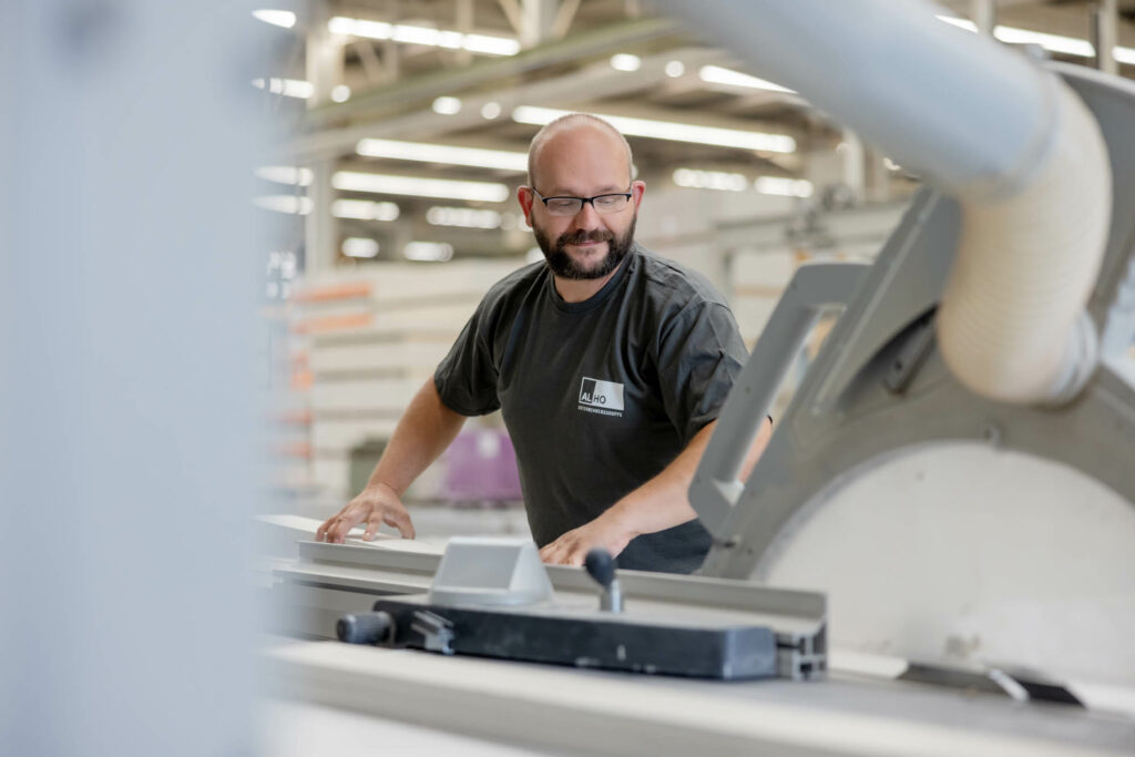Mann mit Glatze, Bart und Brille steht an einer Metallschneidemaschine und schneidet Metall.