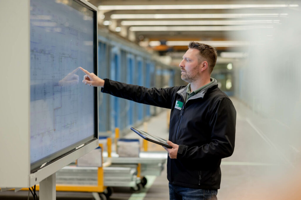 Mann mit kurzen Haaren, schwarzer Jacke tippt auf einem Smartboard.