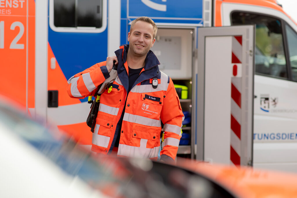 Rettungssanitäter in orangener Jacke vor einem Rettungswagen.