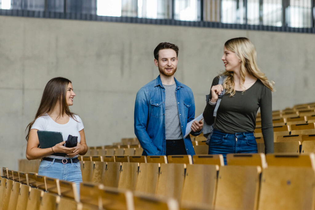 Drei Studenten laufen durch einen Hörsaal.