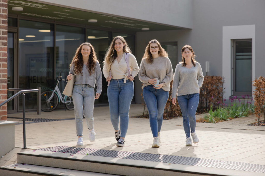 Vier Schülerinnen laufen vor dem Berufschulgebäude lang und lachen.