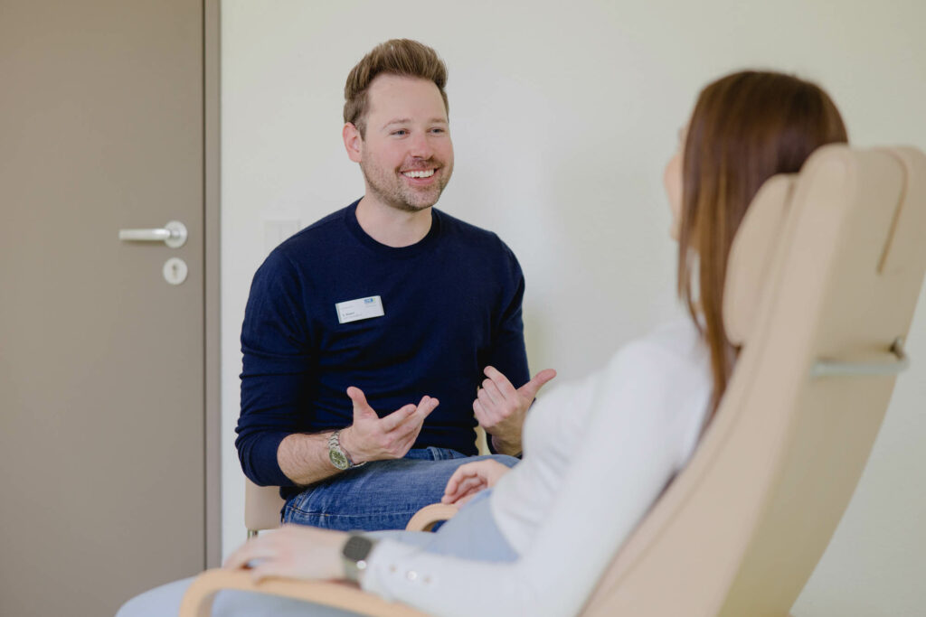 Gesprächssituation, ein Mann erklärt einer Patientin etwas, die auf einem Behandlungsstuhl sitzt.