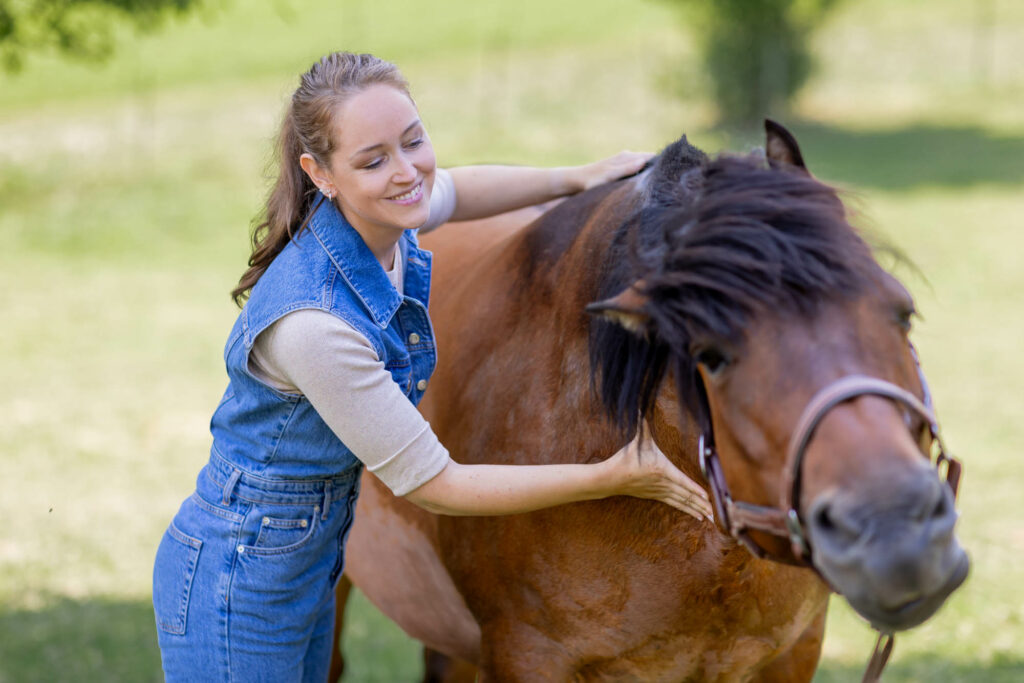 Frau behandelt ein Pferd am Hals. Das Pferd schüttelt sich.