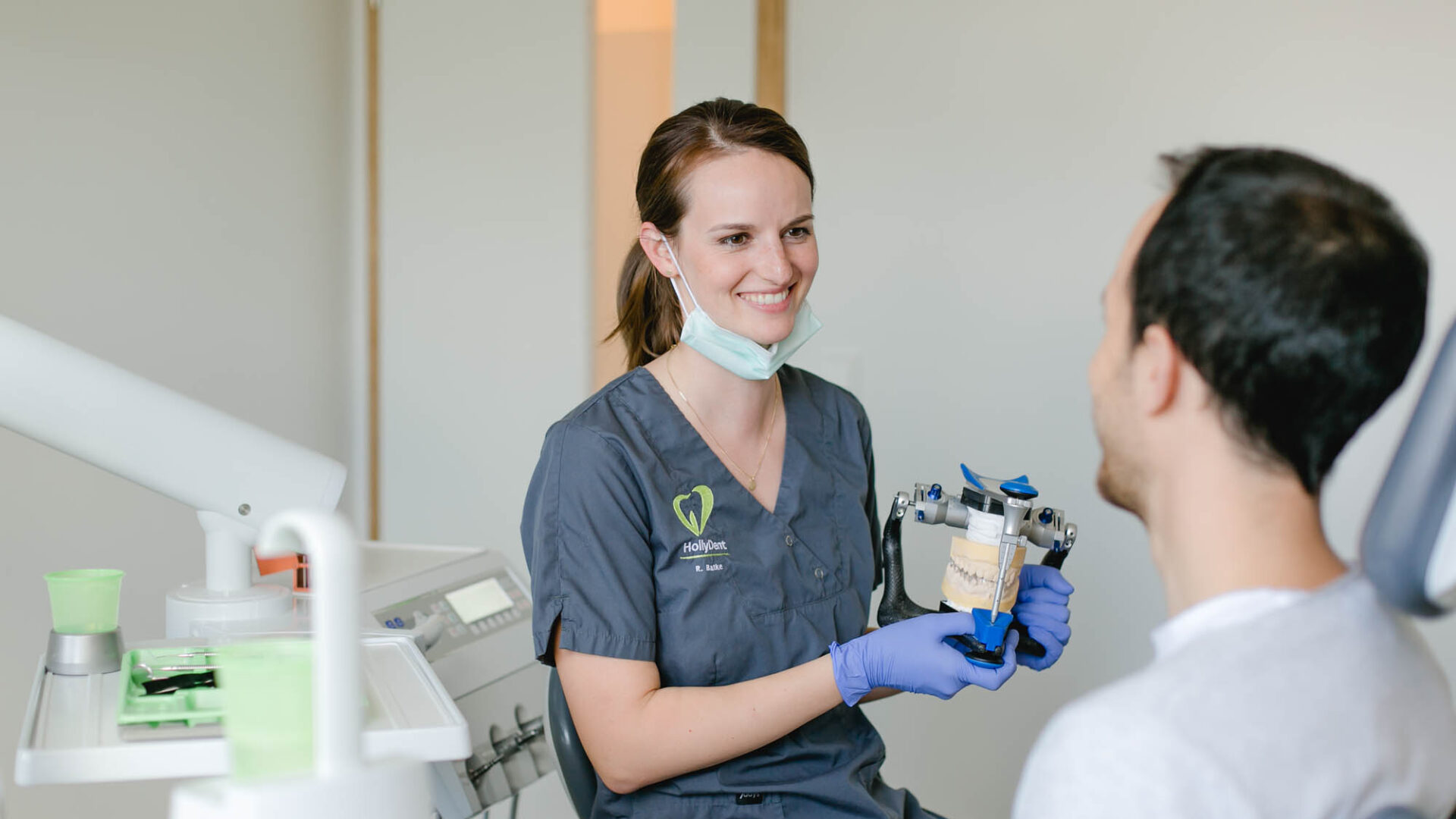 Zahnärztin hat ein Modell in der Hand. Ein Patient sitzt ihr gegenüber.