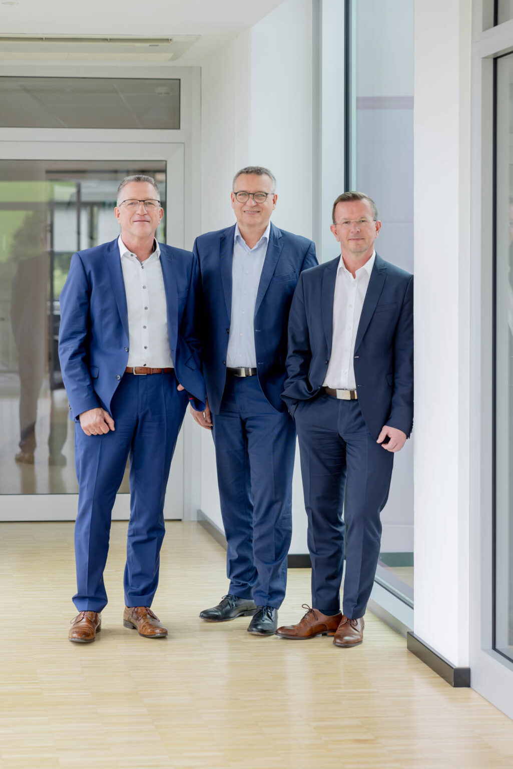 Teamfoto von drei Männer in Anzügen. Sie lachen. Das Bild wirkt seriös, professionell und vertrauensvoll.
