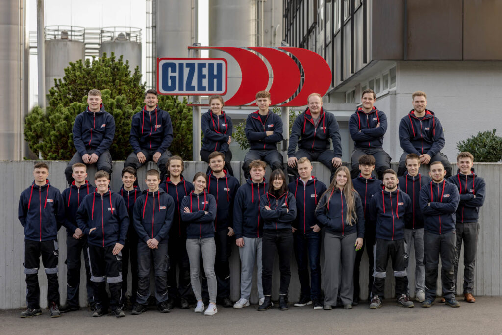 Mitarbeiterfoto der Mitarbeiter von GIZEH. Alle tragen Arbeitskleidung und im Hintergrund ist das Firmenlogo.