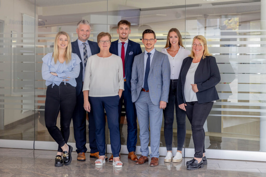 Teamfoto von sieben Personen. Sie stehen in zwei Reihen sind Business-casual gekleidet und lachen.