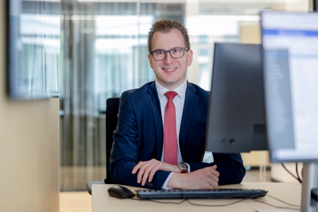 Porträt eines Vermögensberater bei der Volksbank. Er trägt einen Anzug und eine rote Krawatte.