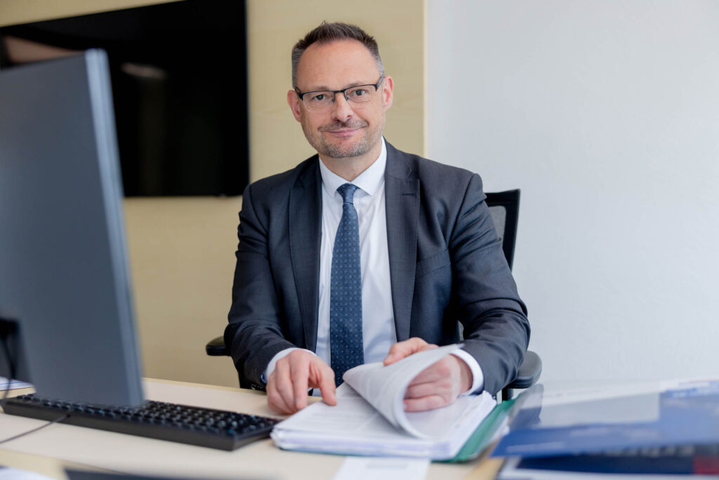 Vermögensberater bei der Volksbank. Er lächelt und blättert in Unterlagen.