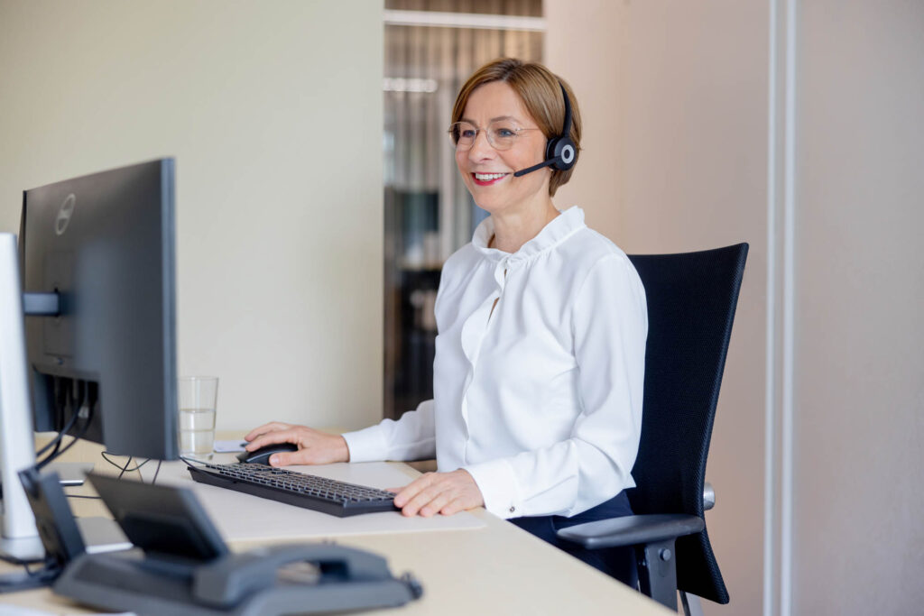Vermögensberaterin bei der Volksbank. Sie sitzt an einem Schreibtisch und trägt ein Headset.
