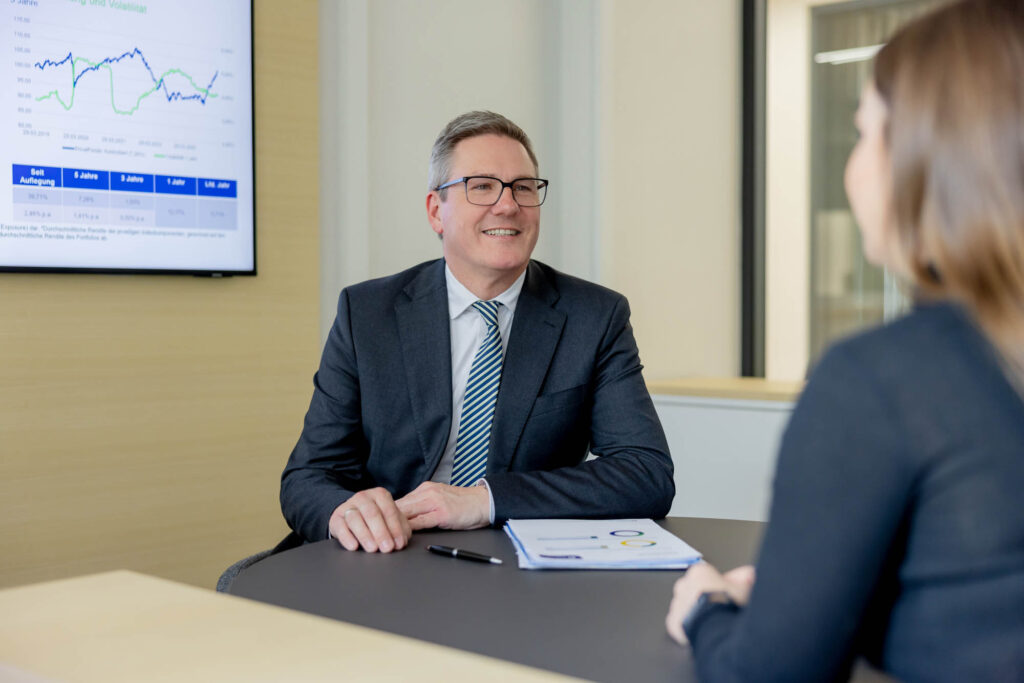 Vermögensberater bei der Volksbank. Er trägt einen Anzug und ihm gegenüber sitzt eine Kundin.
