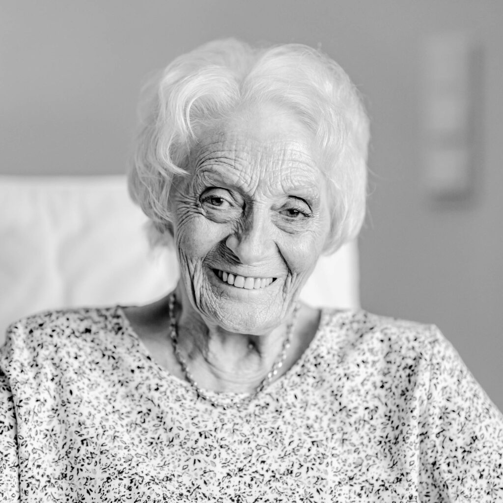 Schwarz-weiß Portrait einer älteren Frau mit kurzen Haaren. Sie lacht.