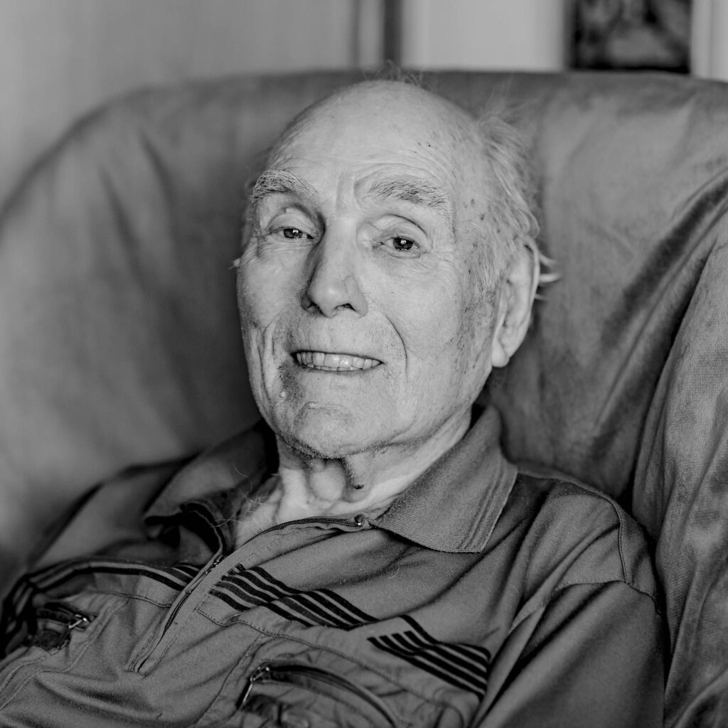 Schwarz-weiß Portrait eines älteren Mannes in einem Sessel. Er lacht.