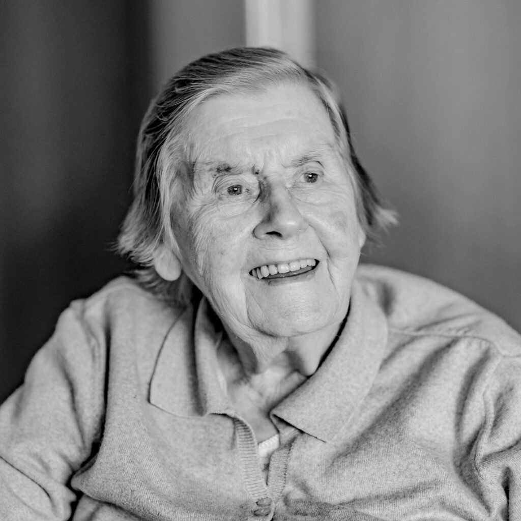 Schwarz-weiß Portrait einer älteren Frau mit Bille, schulterlangen Haaren. Sie lacht.
