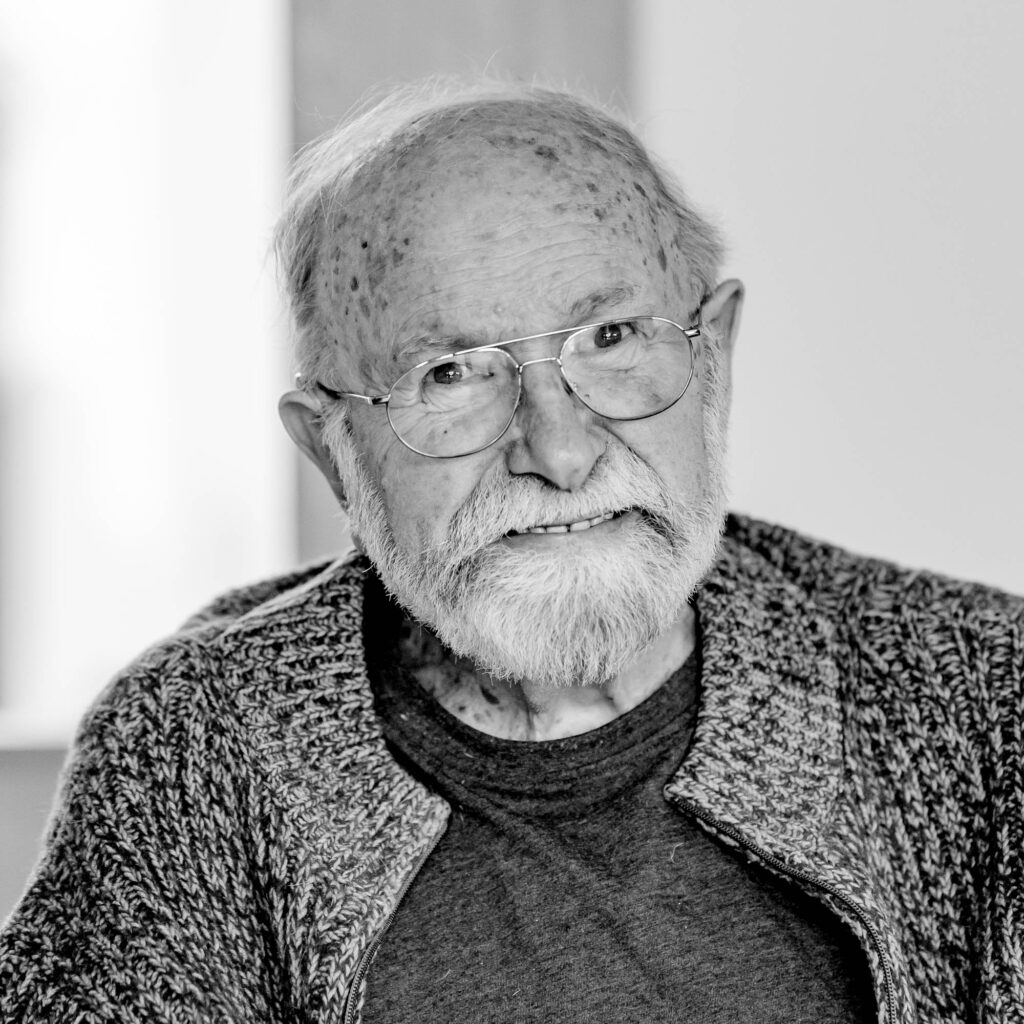 Schwarz-weiß Portrait eines älteren Mannes, mit Glatze, Bart und Brille. Er lacht.