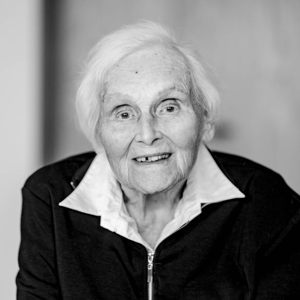 Schwarz-weiß Portrait einer älteren Frau mit kurzen Haaren und Brille. Sie lacht.