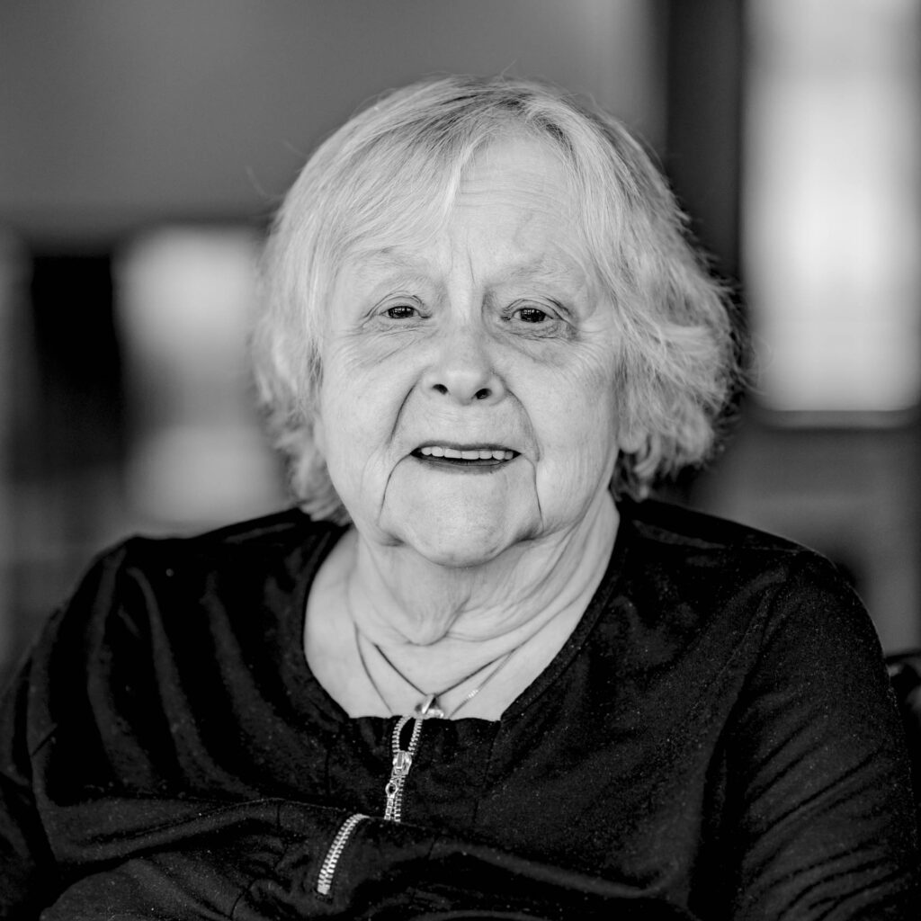 Schwarz-weiß Portrait einer älteren Frau mit schulterlangen Haaren. Sie lächelt.
